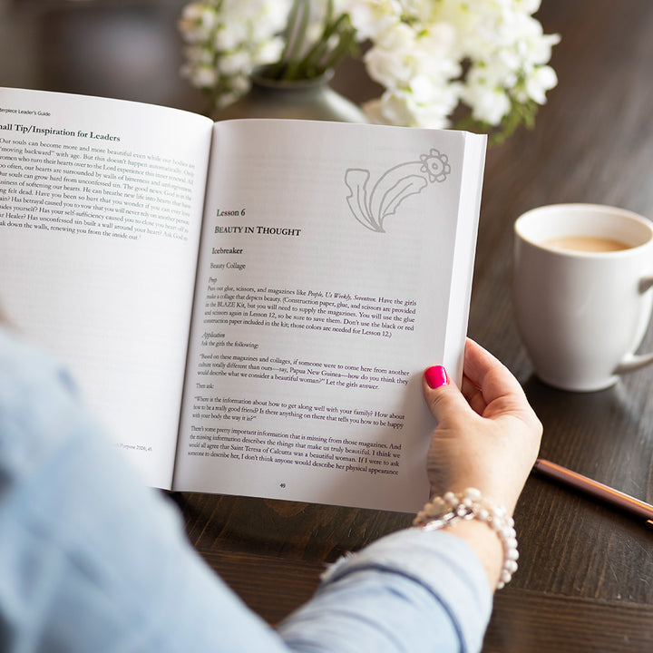 woman holding BLAZE Masterpiece leader's guide, inside pages, at table
