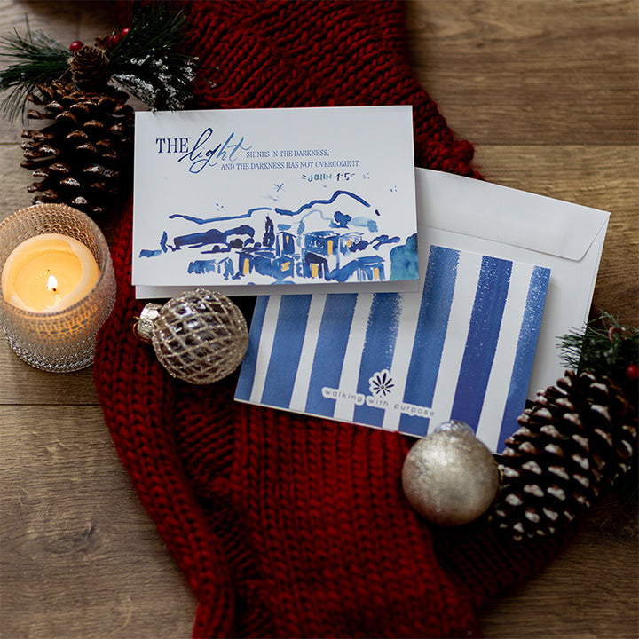 The Walking with Purpose Limited Edition Christmas Card Set features beautiful watercolor artwork in blues and yellows and the verse John 1:5: “A light shines in the darkness, and the darkness has not overcome it.” The back cover has blue stripes.