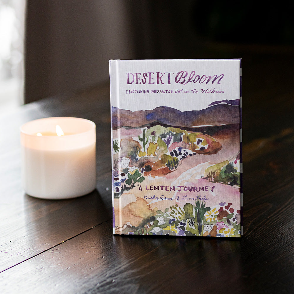 Book titled 'Desert Bloom' on a wooden surface with a candle in the background