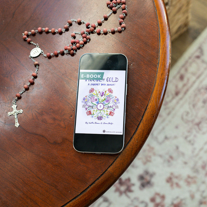 Phone displaying an e-book titled 'House of Gold: A Journey into Advent' on a wooden table with a rosary.
