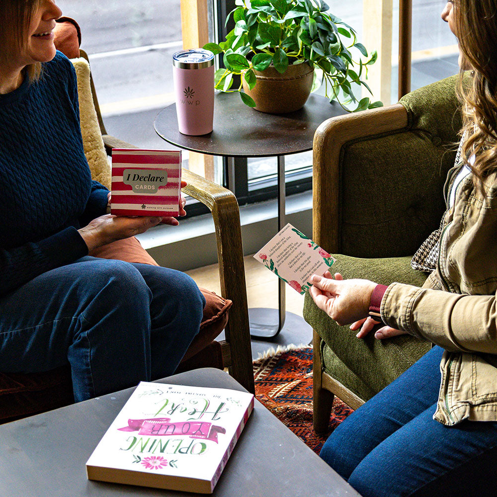 Two people sitting in a cozy room with a Box of 'I Declare' Scripture cards and a pink Walking with Purpose tumbler.