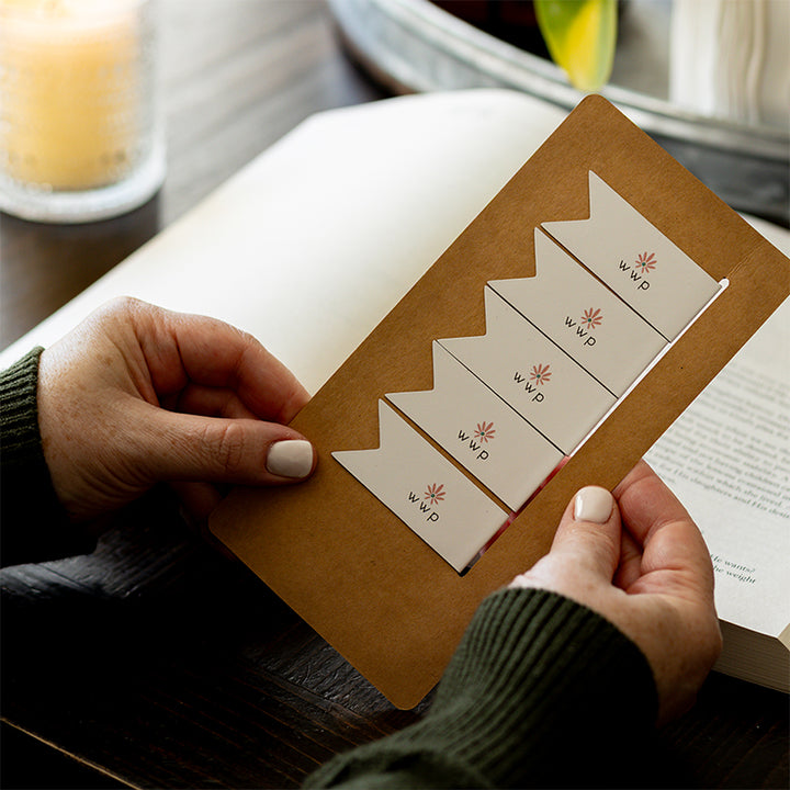 Walking with Purpose Magnetic Bookmarks designed with the signature WWP flower logo. Woman is holding card with five bookmarks with Bible study and plant in the background.