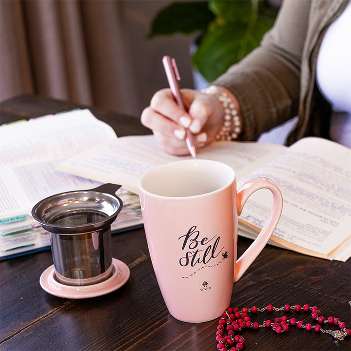 Light pink Be Still Tea Mug with Infuser and Lid on a table with a woman doing a Bible study