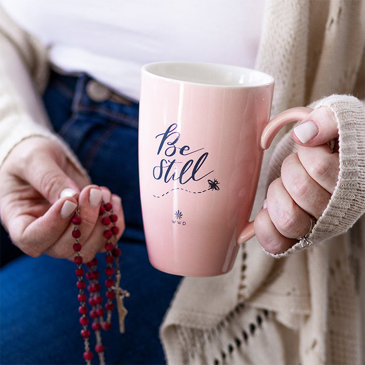 A woman holding a Light pink Be Still Tea Mug with Infuser and Lid and rosary