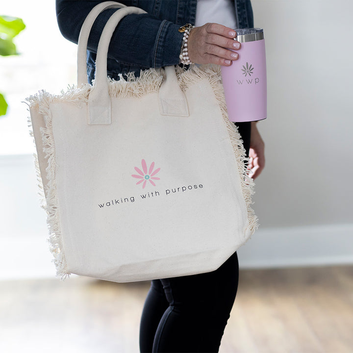 Woman carrying Pink tumbler with WWP flower logo and WWP logo fringe bag