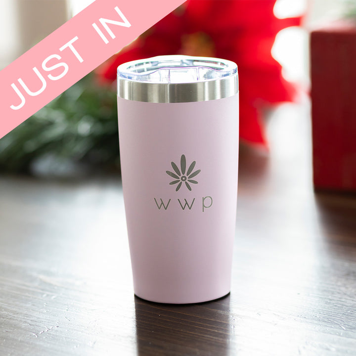 Pink tumbler with WWP flower logo on wooden table with Just In banner