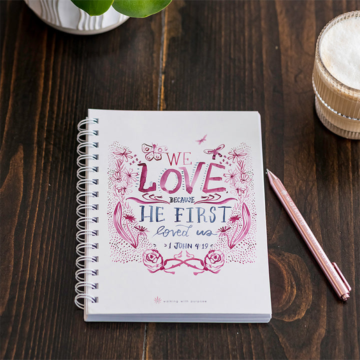 A white spiral-bound notebook with pink and blue decorative text reading &