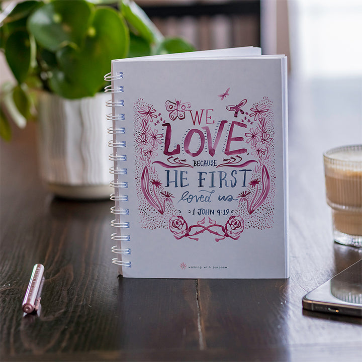 A spiral-bound journal with a white cover featuring pink and blue hand-lettered artwork and the quote &